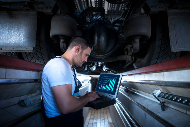 Technician working on analytics from a laptop beneath a vehicle.